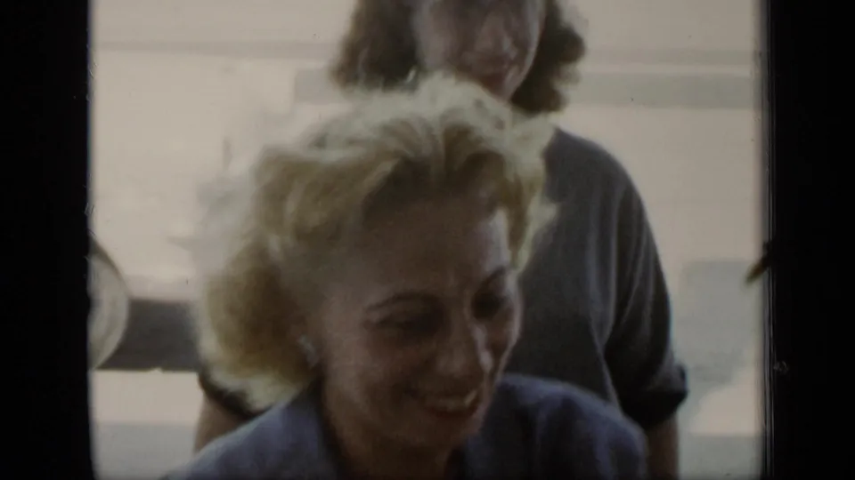 A blonde woman smiles close to the camera as another woman stands behind her in sunlit 1948 New York home-movie footage.