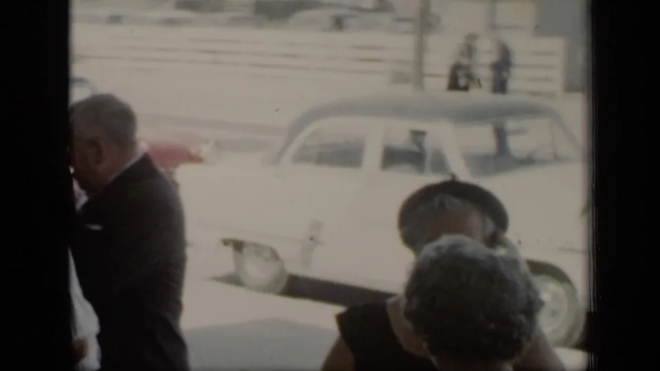 Adults in formal mid-century clothing move along the street near a pale parked car in the 1948 New York clip.