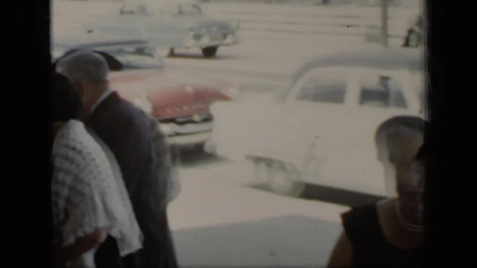 The closing frame shows adults near classic cars on a bright New York street, with the view partly blocked by dark framing.