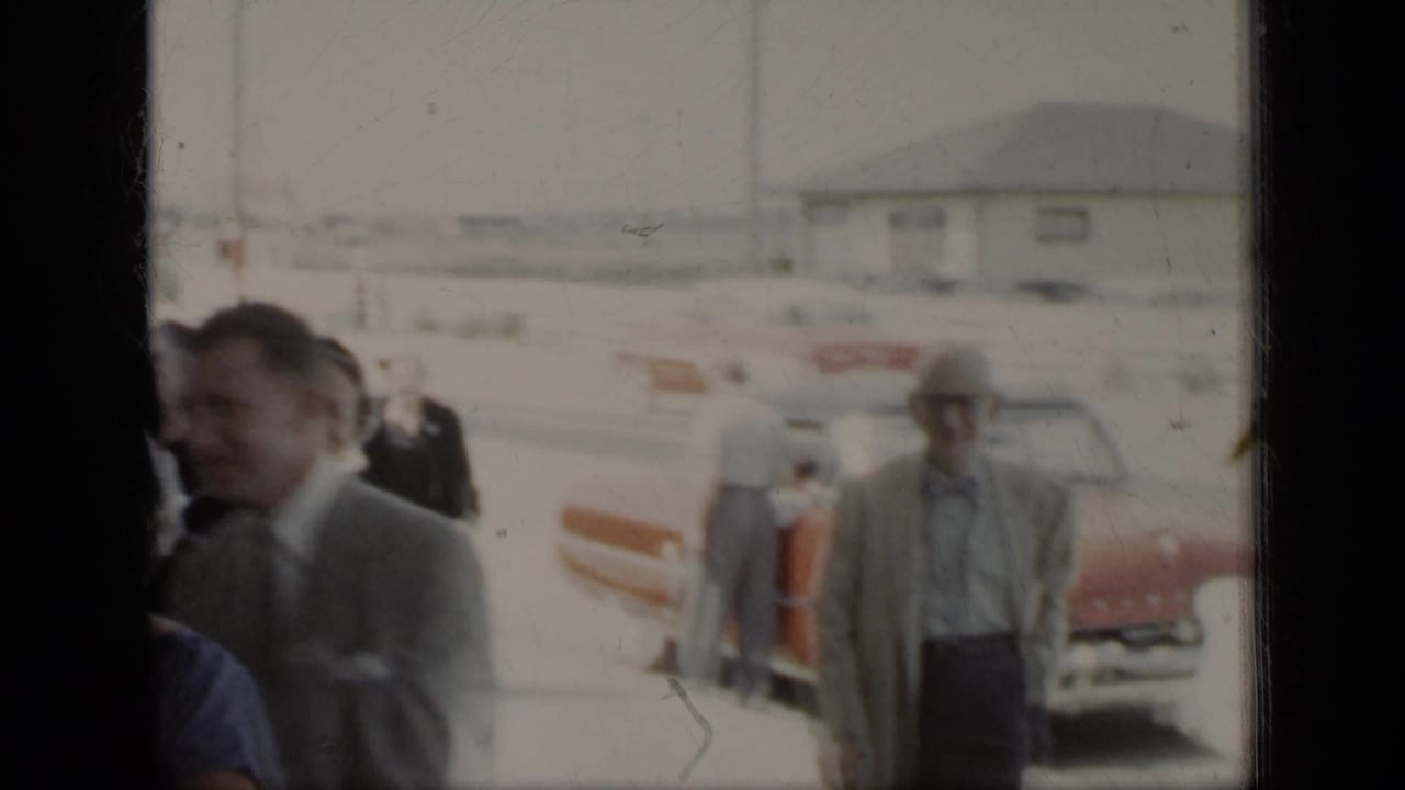 Adults walk near a red car in bright outdoor light, seen through soft 8mm framing.