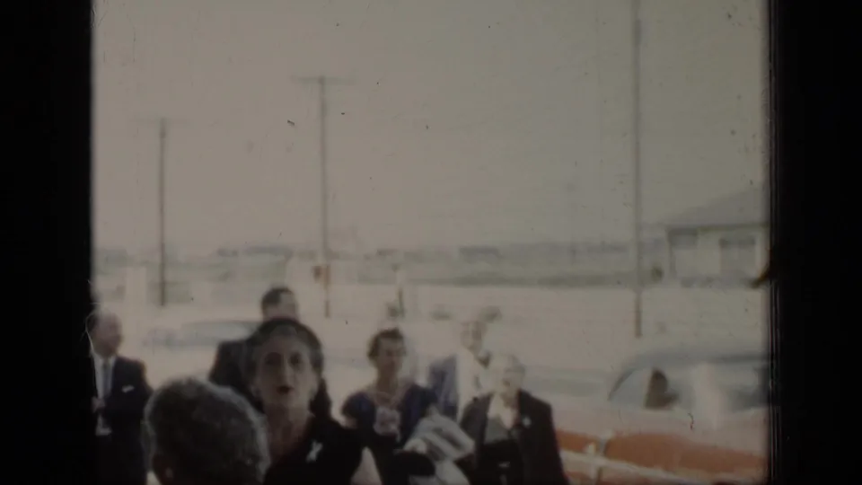 In New York 1948 home-movie footage, formally dressed adults gather outdoors near cars, pavement, and utility poles.