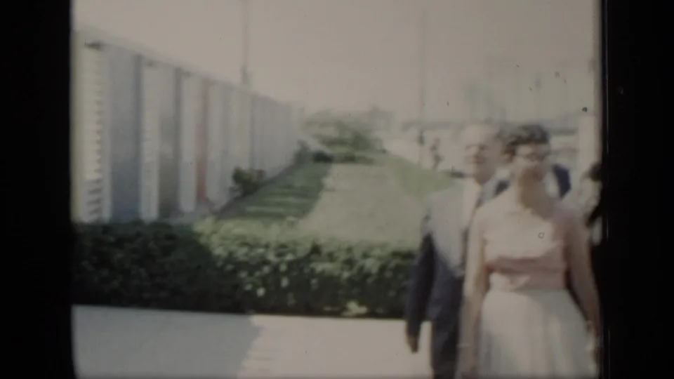 The wedding couple appears at the right edge of the 1948 New York frame, passing a hedge, walkway, and long building wall.