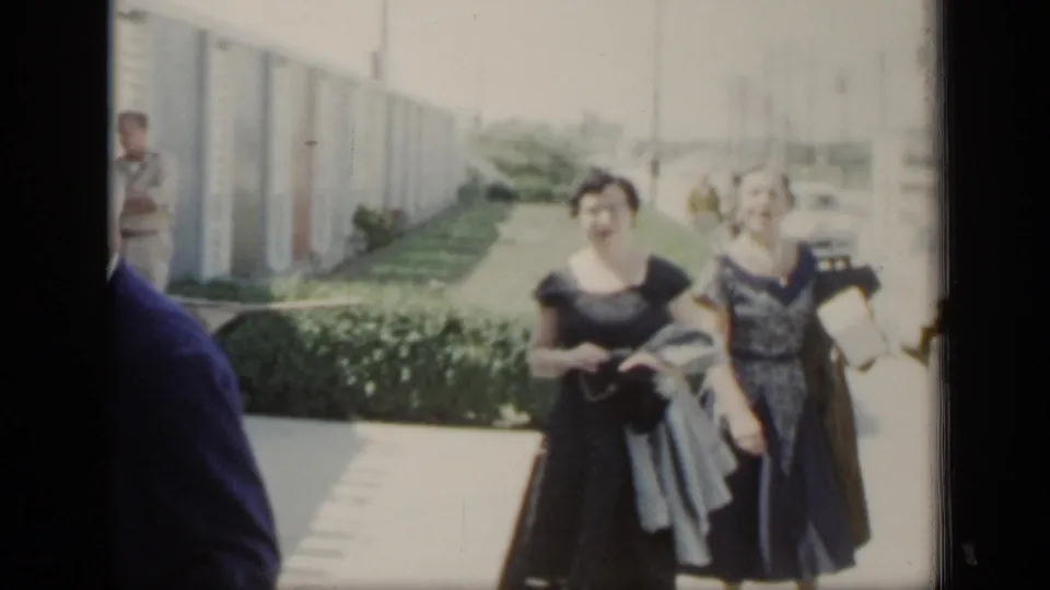 Two women in elegant dark dresses walk along a hedge-lined outdoor path in the 1948 New York home-movie clip.