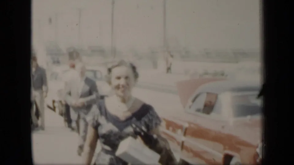 A woman in a dark patterned dress and pearl necklace walks toward the camera on a New York street in 1948 footage.