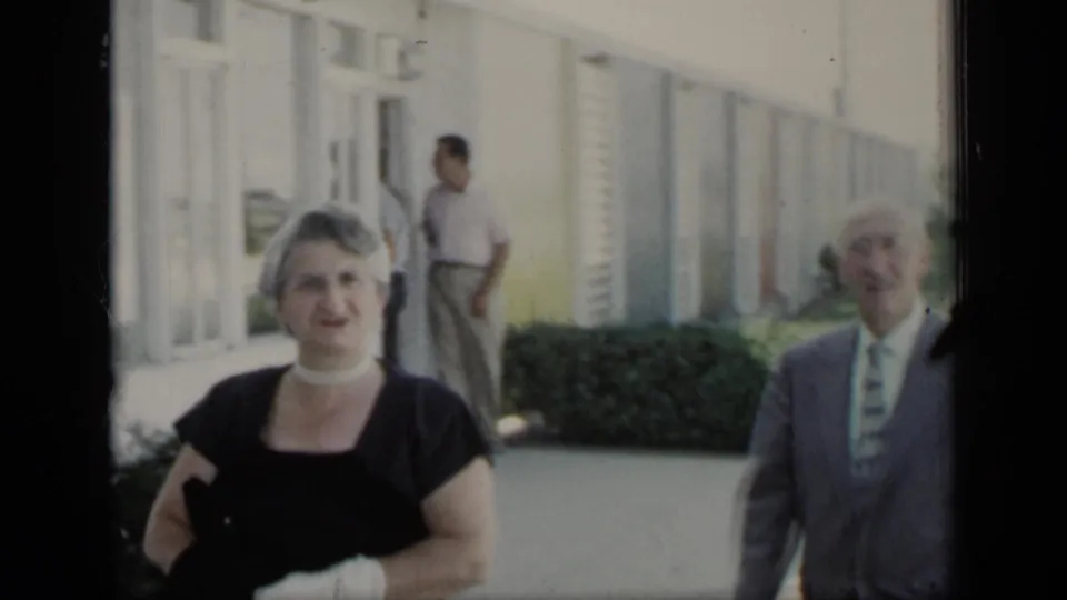 A woman in white gloves and an older man in a suit pass the camera outside a building in 1948 New York home-movie footage.