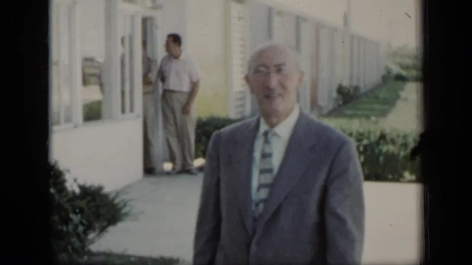 An older man in a gray suit and striped tie smiles toward the camera outside a New York building in 1948 home-movie footage.