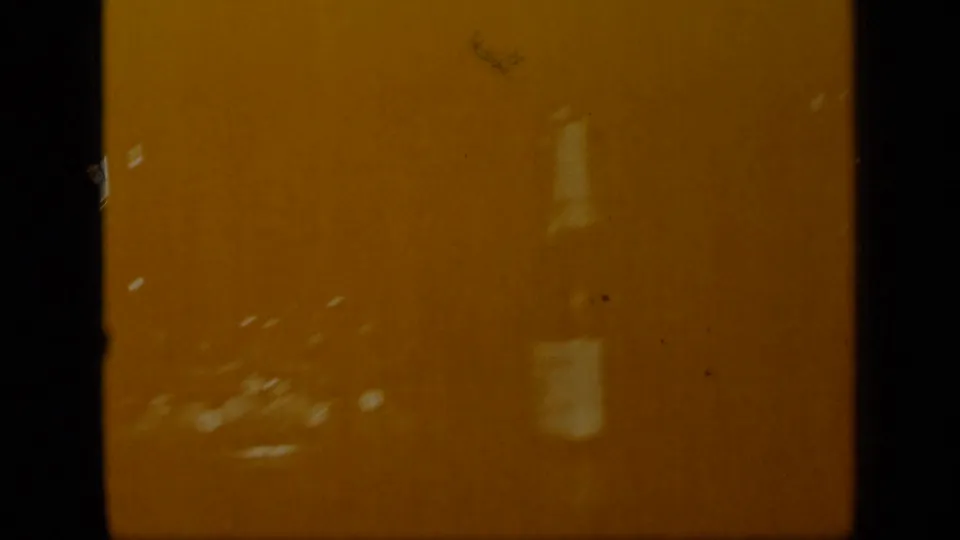 Amber-toned transitional 8mm frame with faint, indistinct forms and visible dust or scratches.