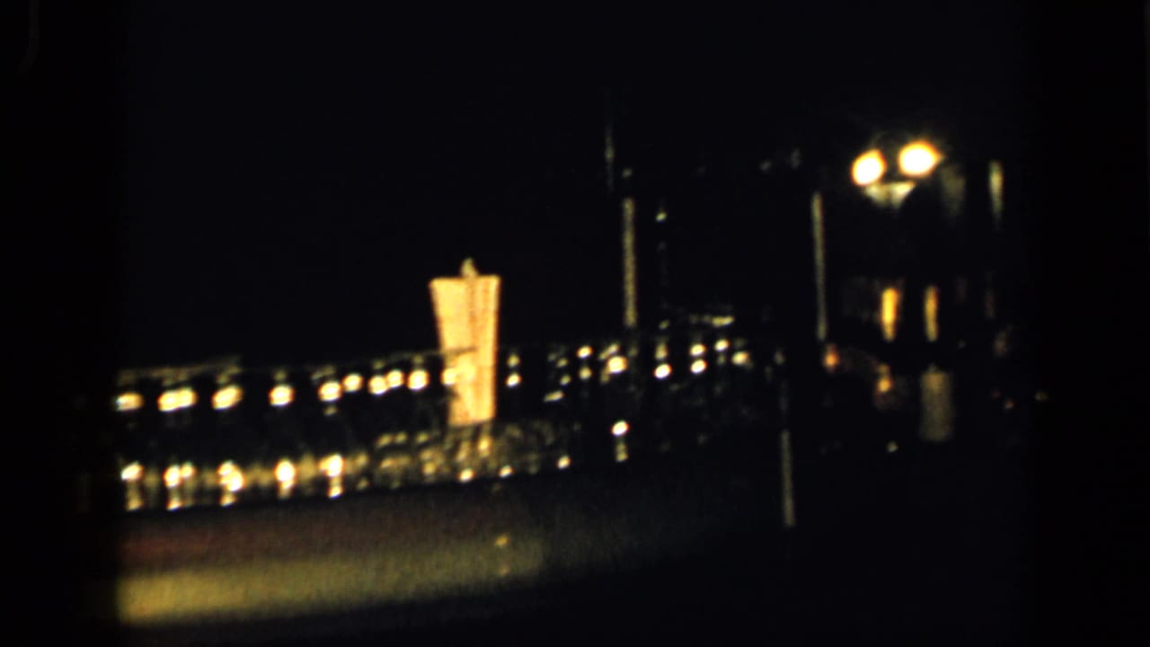 Dim nighttime bridge or waterfront lights seen across a dark urban scene.