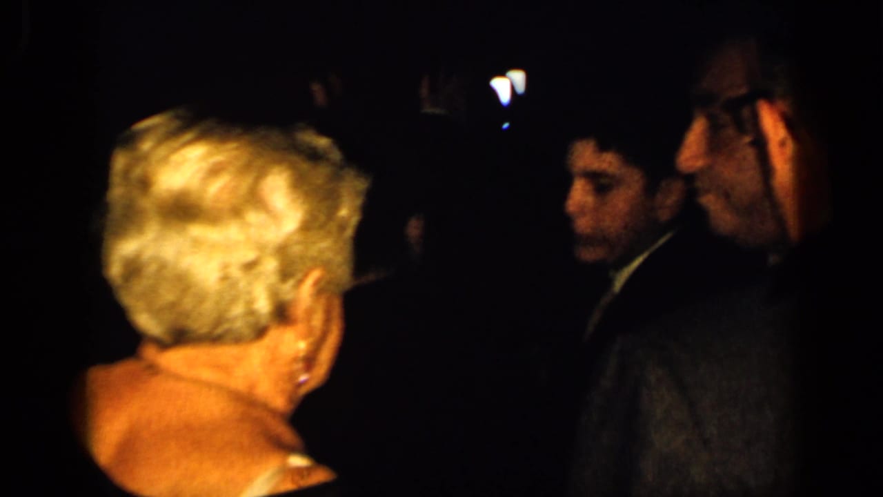 Blonde woman seen from behind near men in dark formal wear.