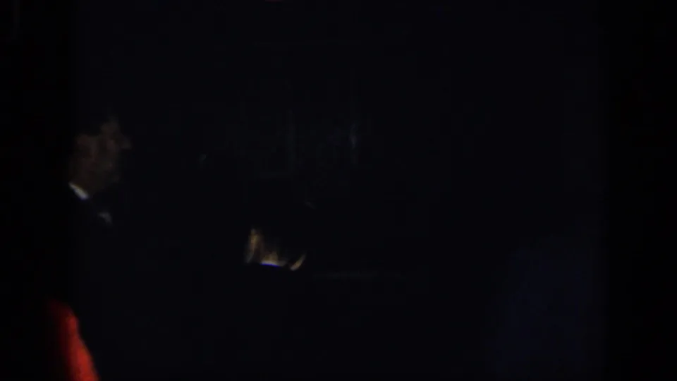 A low-light 1948 New York home-movie frame shows partially obscured formal guests in a dark interior.