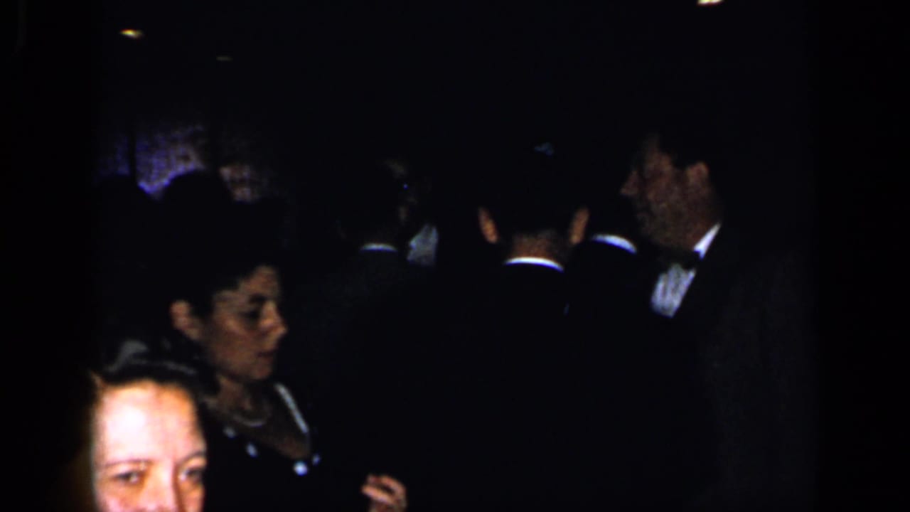 Dim formal party with adults in evening dress and a man in a tuxedo.