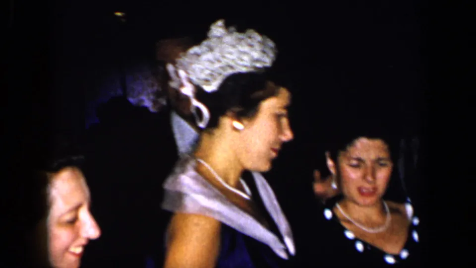 1948 New York frame with a woman in a tiara-like headpiece and evening gown moving through a crowded formal room.