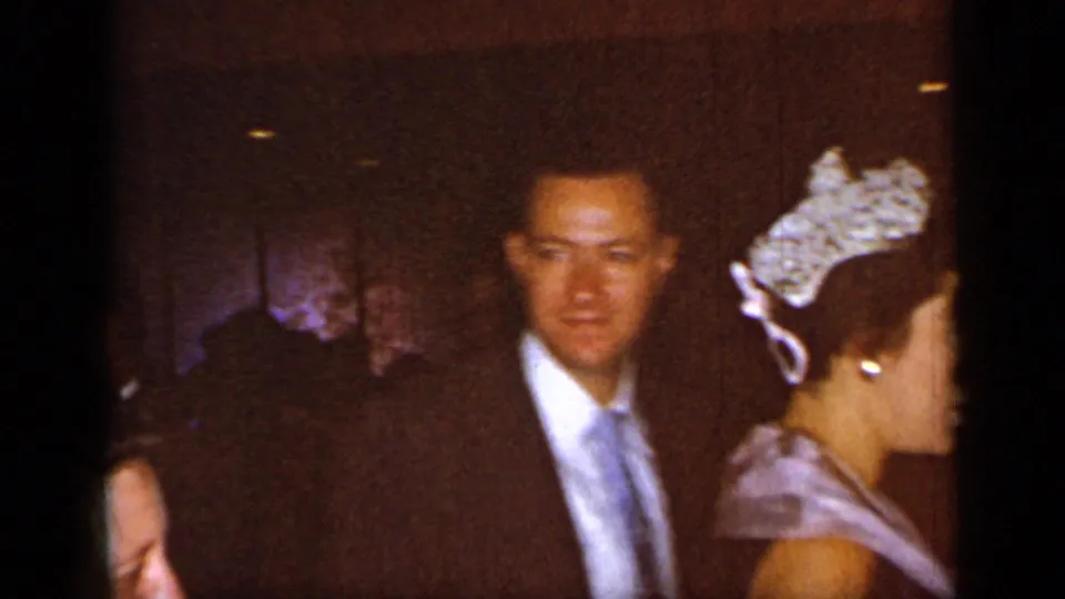 1948 New York home-movie frame showing a suited man beside a woman in a tiara-like headpiece during a formal gathering.