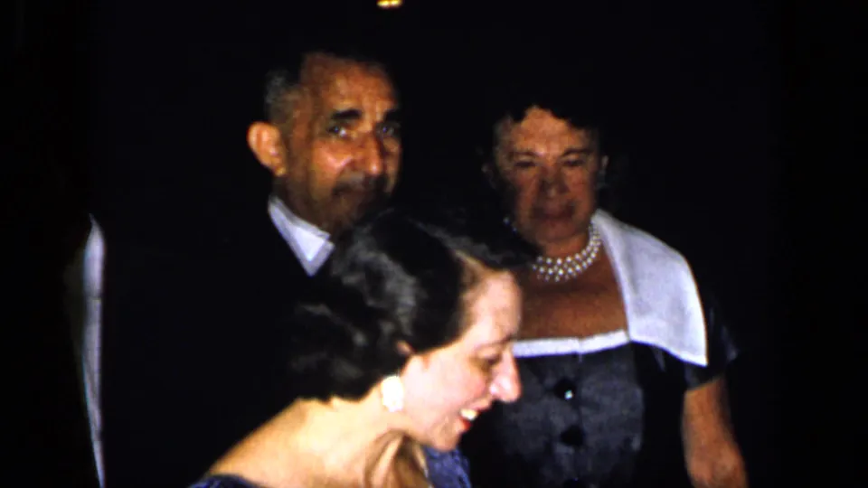 A smiling woman appears in the foreground while other formally dressed adults stand behind her in the dim 1948 New York party scene.