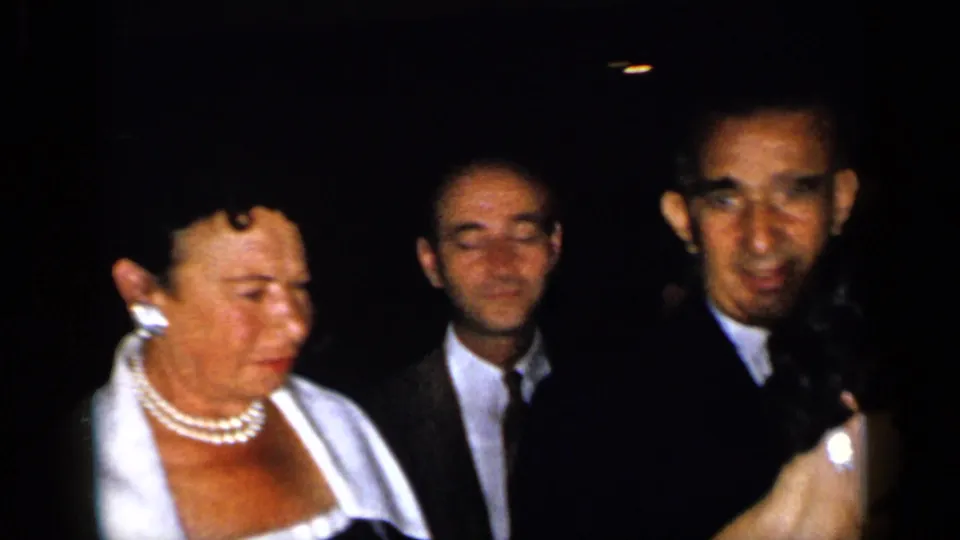 Close 1948 New York home-movie view of formal party guests, with a pearl-wearing woman and suited men near the camera.