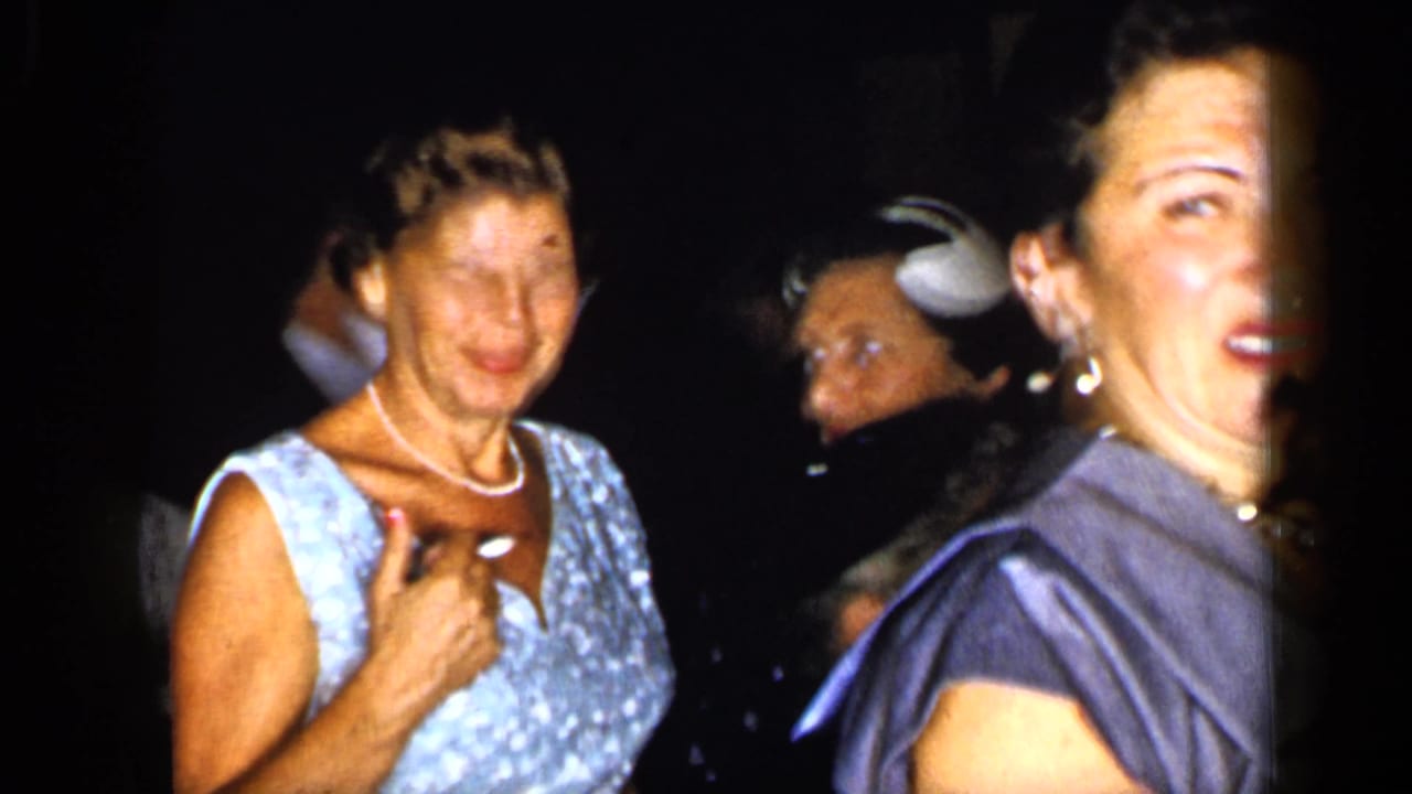 Woman in a light patterned dress smiles beside other adults in a dark corridor.