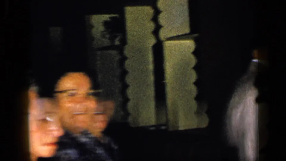 Blurred figures in formal clothing pass through a dark corridor, with 8mm motion blur and warm exposure shaping the candid scene.