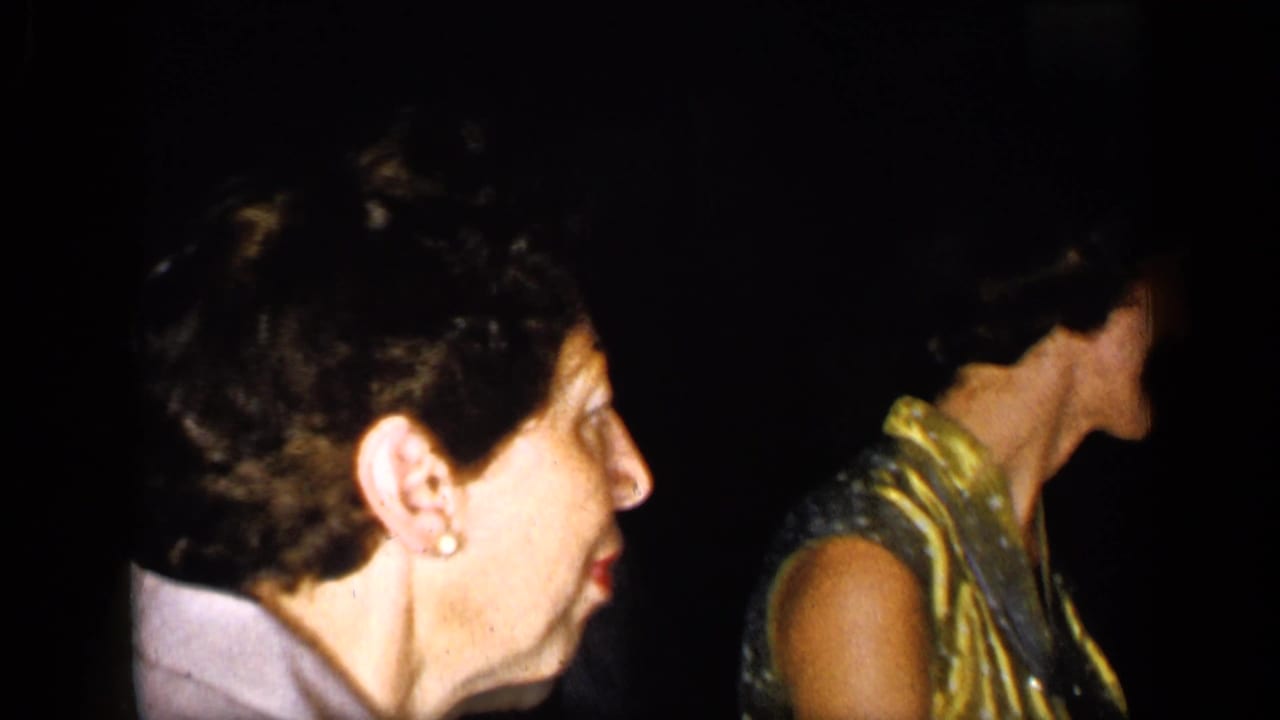 Woman in profile beside another adult in a dark, crowded room.