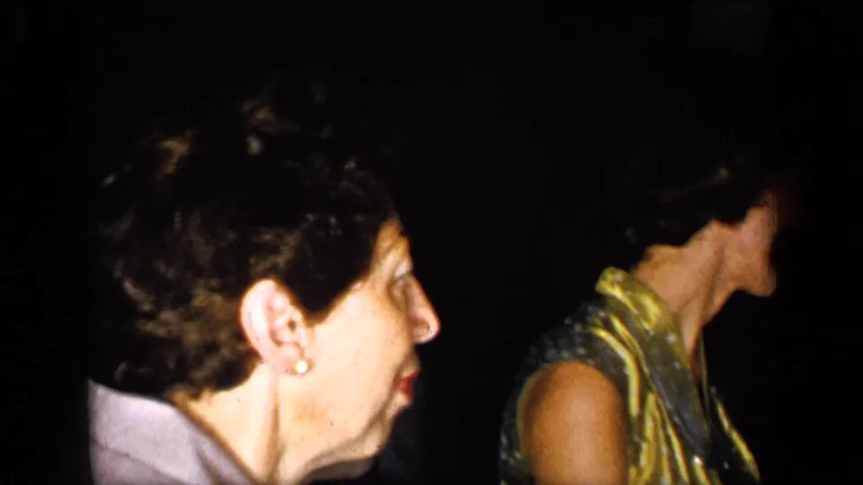1948 New York home-movie frame showing a woman in profile with pearl earrings near another formally dressed adult in a dim room.