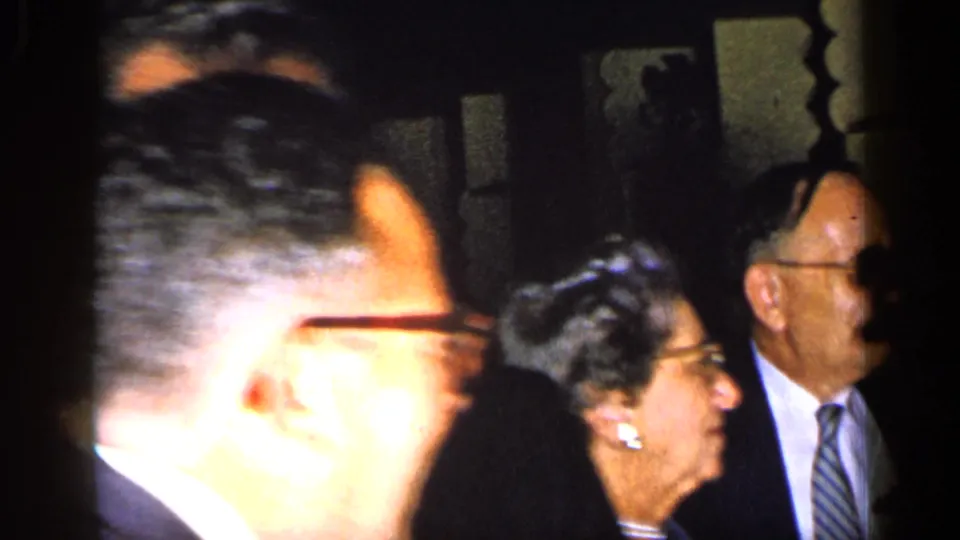 Close 1948 New York home-movie view of adults in suits and jewelry gathered in a dim interior.