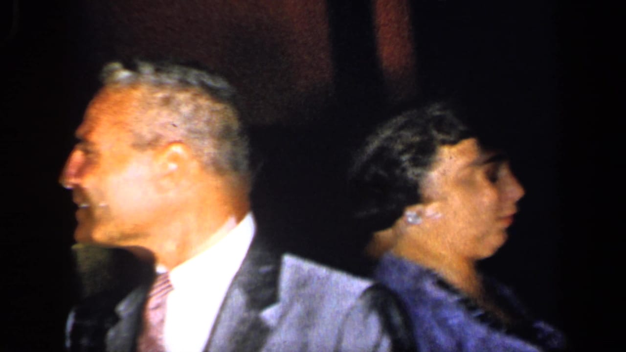 Man in a suit seen in profile beside a woman in dark formal clothing.