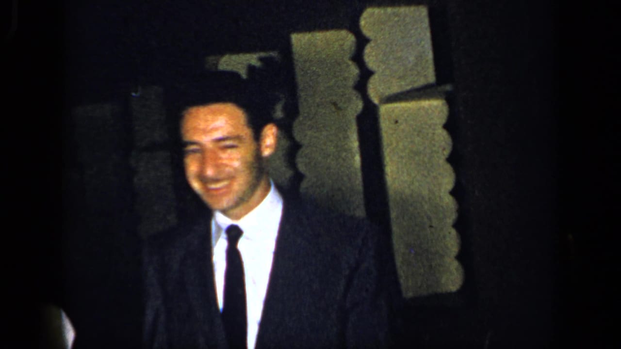 1948 New York frame of a smiling adult man in a dark suit and tie near decorative interior trim.