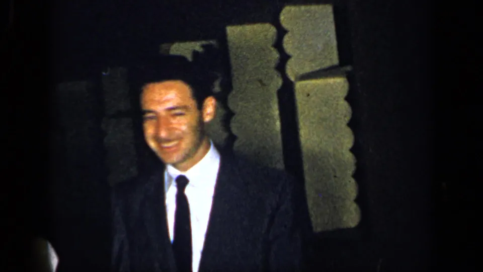 1948 New York frame of a smiling adult man in a dark suit and tie near decorative interior trim.