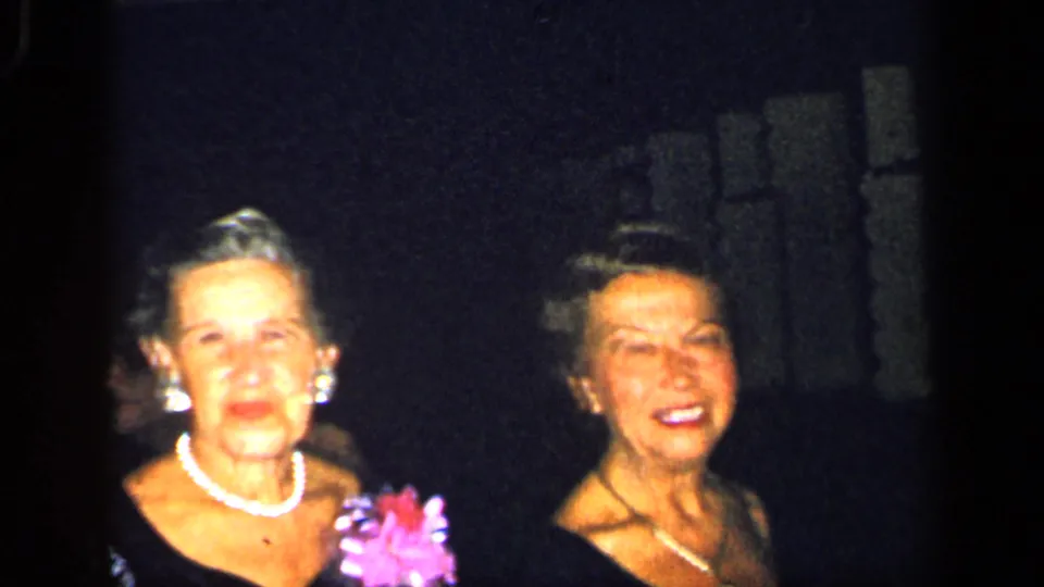 Two adult women at a New York 1948 formal gathering appear in dark dresses with pearl-like jewelry, one holding a pink flower accessory.