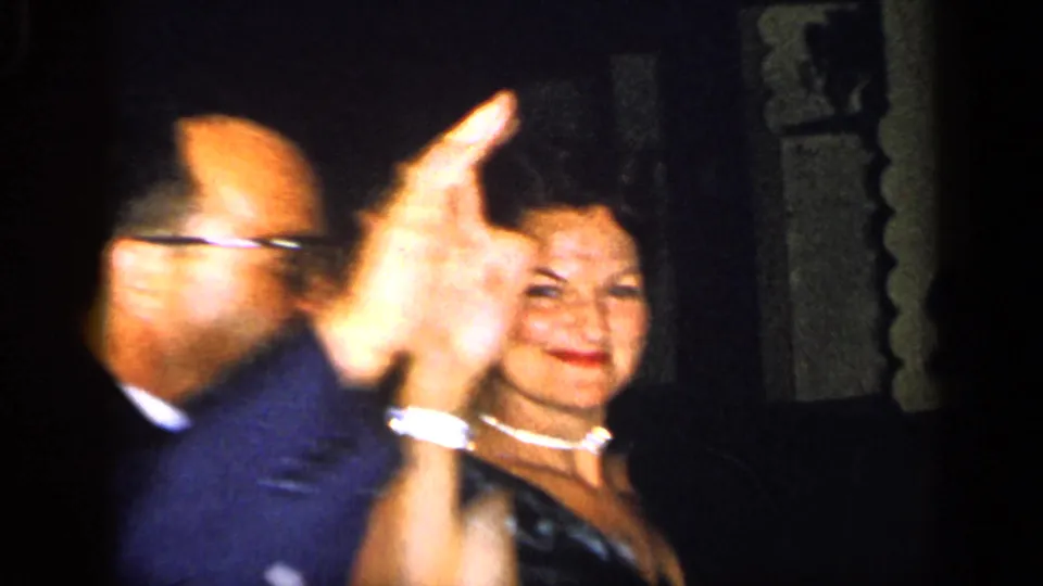 At the New York 1948 gathering, a man with glasses gestures near a smiling woman wearing a dark dress and necklace.