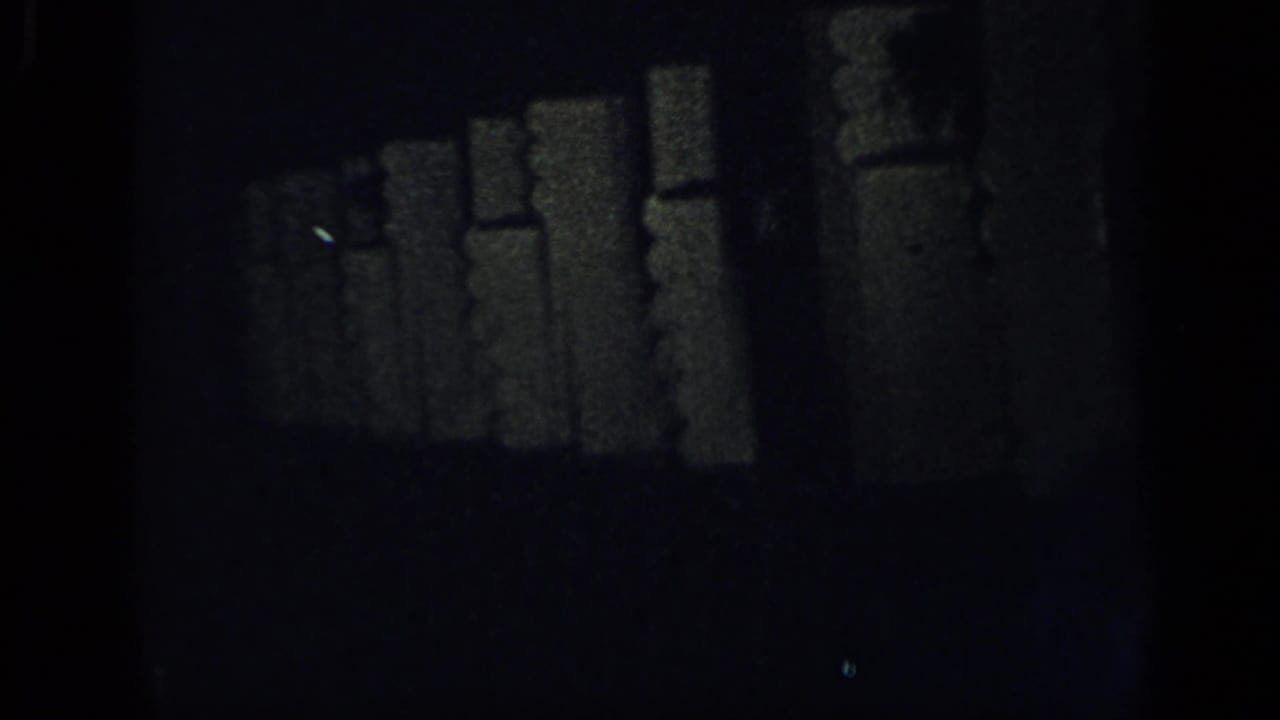 Dark, underexposed frame with indistinct interior shapes and film edges.