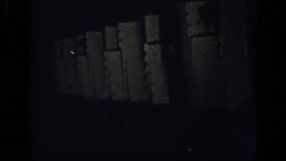 Underexposed 8mm frame from the 1948 New York clip, with dark interior shapes and heavy film grain but no clear faces.