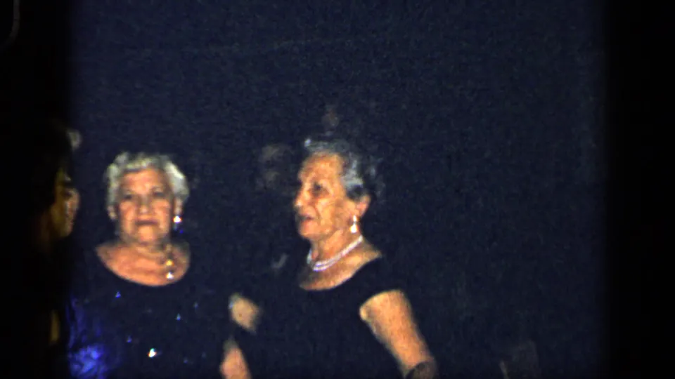 Two older women in dark formal dresses and pearl necklaces stand together at a dim 1948 New York evening gathering.