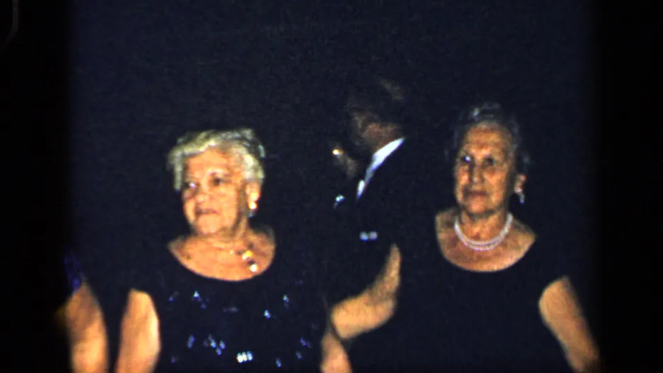 Two older women in formal dresses stand near a man in a dark suit during the 1948 New York home-movie event.
