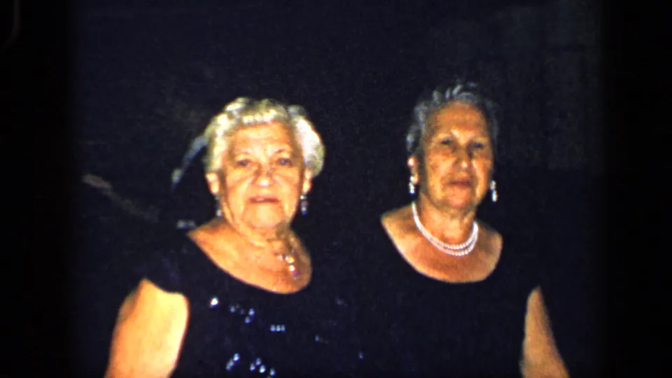 Two older women in black dresses and pearl necklaces face the camera in a dim 1948 New York formal-event frame.