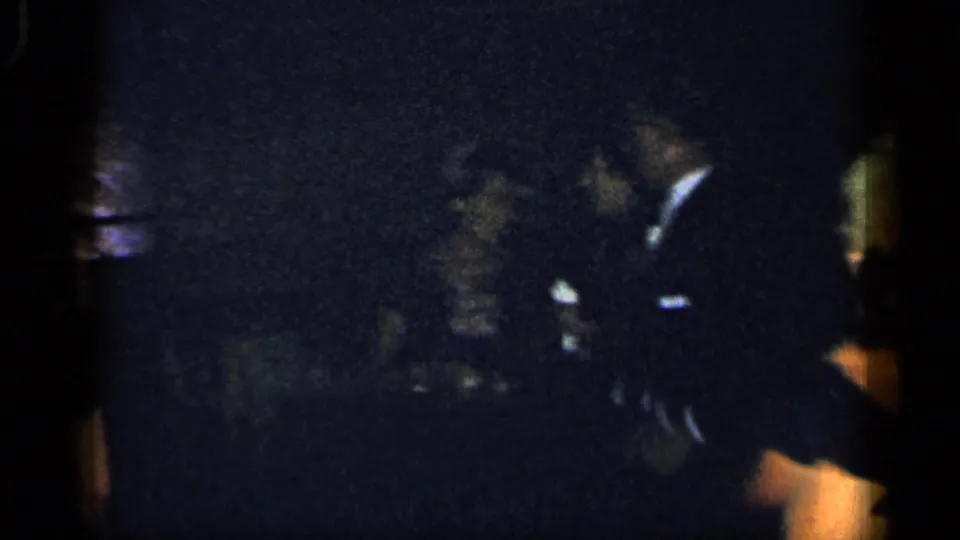 1948 New York 8mm frame showing adults in formal attire gathered in a dark interior, partly obscured by exposure and framing.