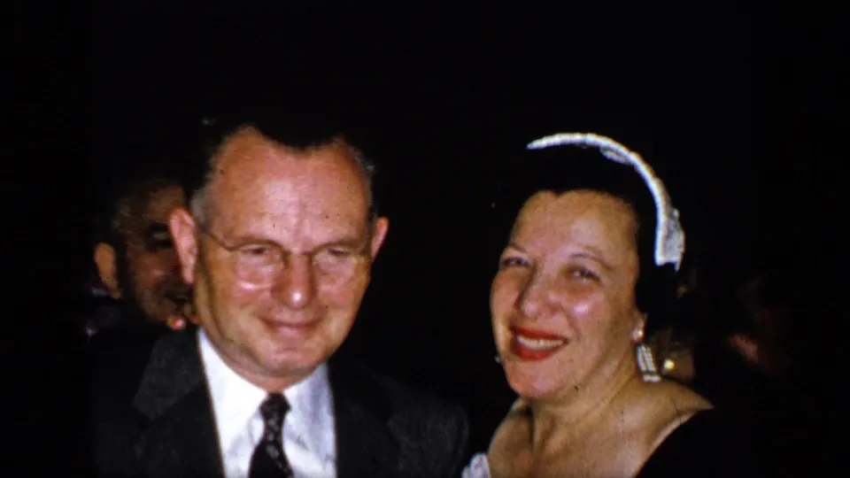 A suited man and smiling woman in a formal headpiece face the camera together in the 1948 New York home-movie clip.
