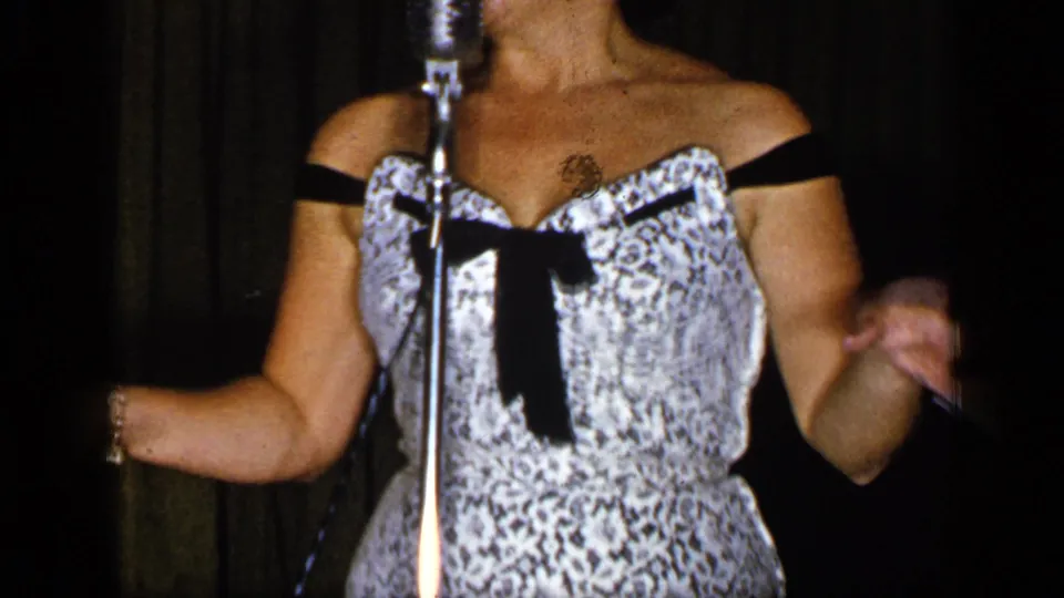 The performer stands at the microphone in a patterned dress, gesturing with both hands during the brief 1948 New York stage scene.