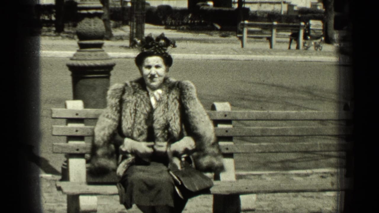Woman faces the camera from a park bench, wearing a fur stole and hat.