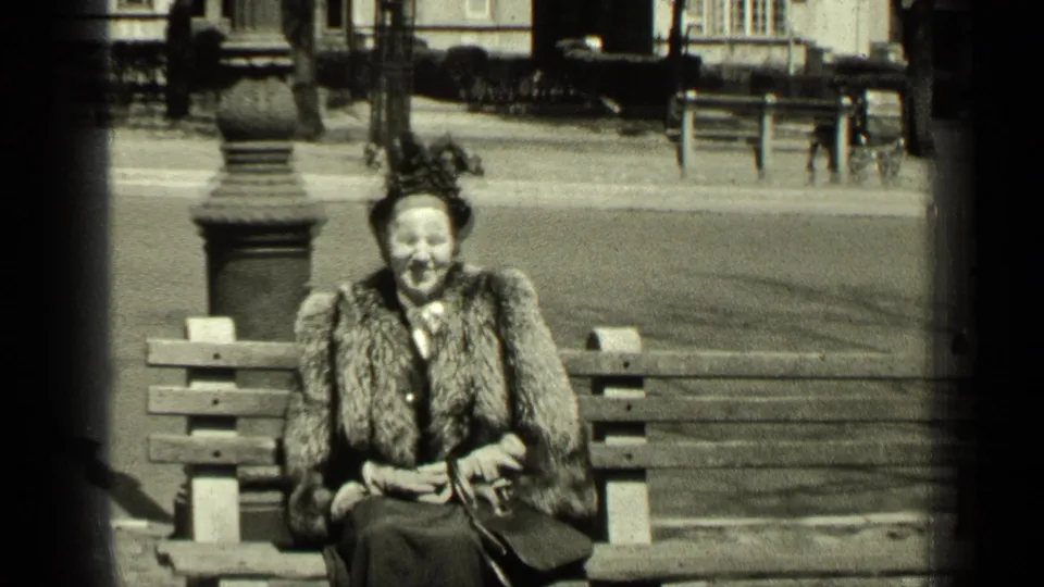 The clip ends with the woman smiling on the bench, her fur stole, hat, gloves, and handbag clearly visible in the 8mm frame.