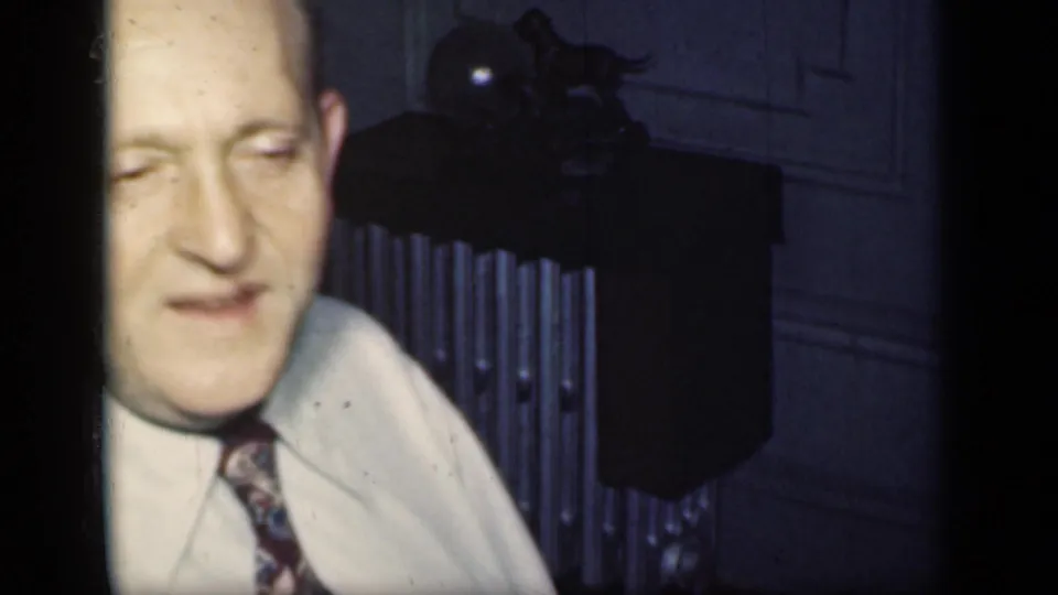 A man in a light shirt and patterned tie appears beside a radiator in a dim 1949 New York private interior.
