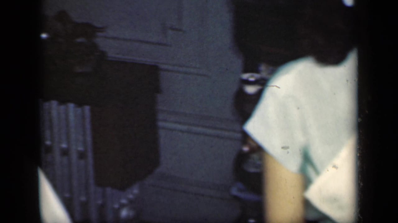 Adult woman partly cropped in a dim interior, with radiator and wall panels visible.