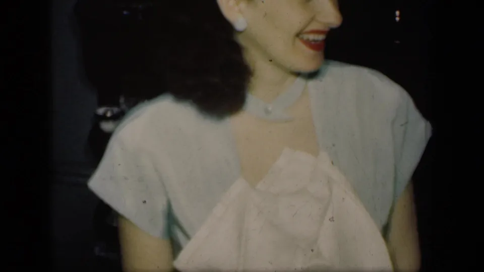 A woman in light clothing turns to the side and smiles during a 1949 New York indoor home-movie gathering.