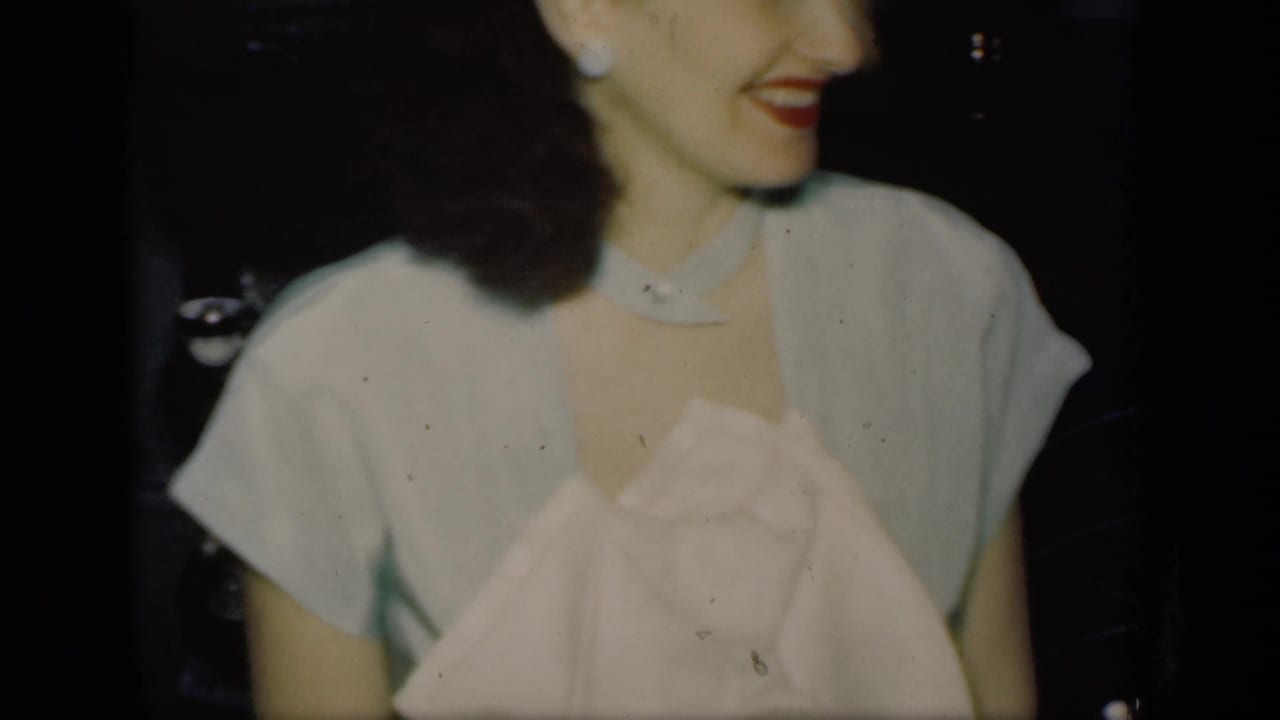 Smiling woman in a light dress seated at a dim dinner table.