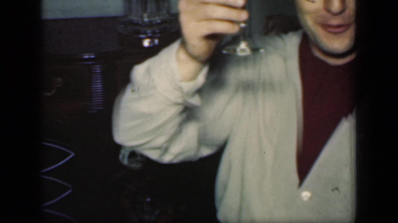 A man in a light cardigan over a dark turtleneck raises a wine glass toward the camera in 1949 New York footage.