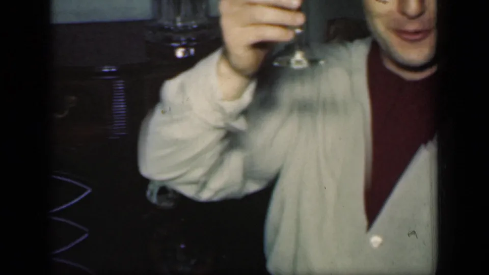 A man in a light cardigan over a dark turtleneck raises a wine glass toward the camera in 1949 New York footage.