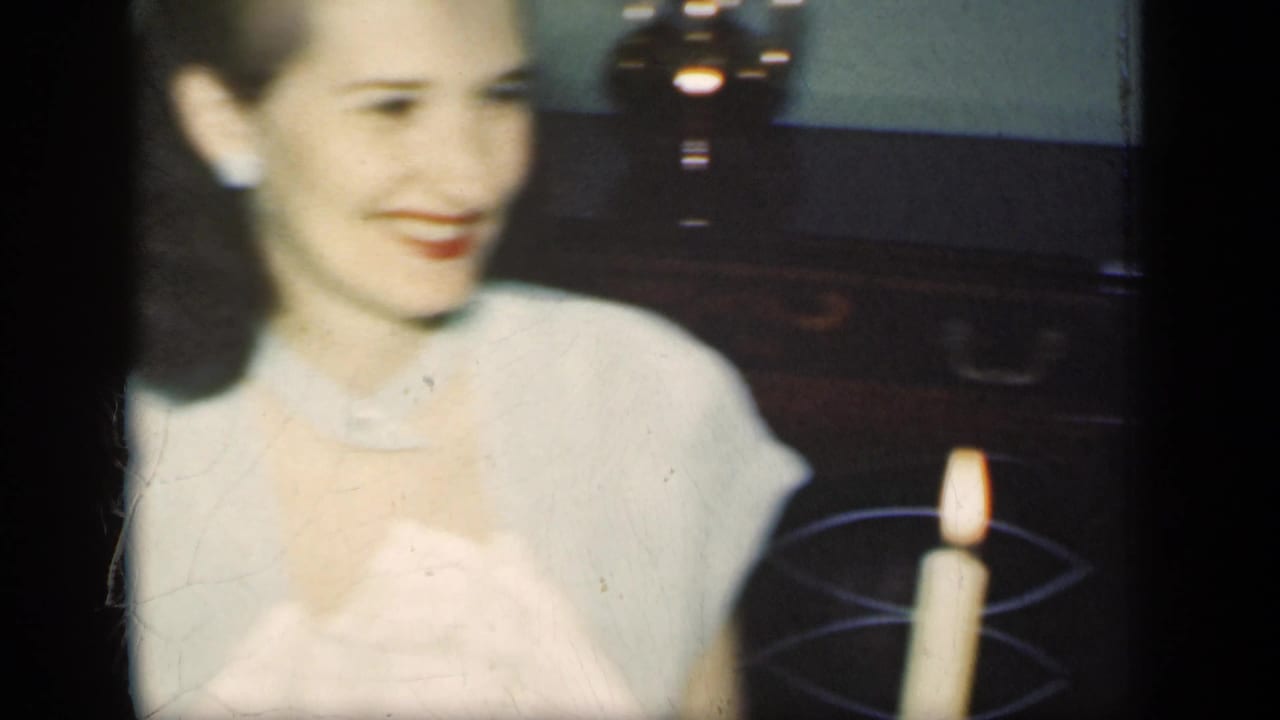 A woman in a light-colored dress smiles beside a lit candle in a private New York interior, based on the 1949 clip metadata.