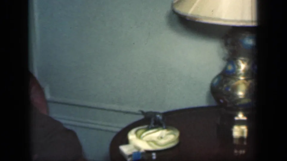 The camera has panned across the 1949 New York interior to a side table with a decorative lamp, coiled cord, and small tabletop items.