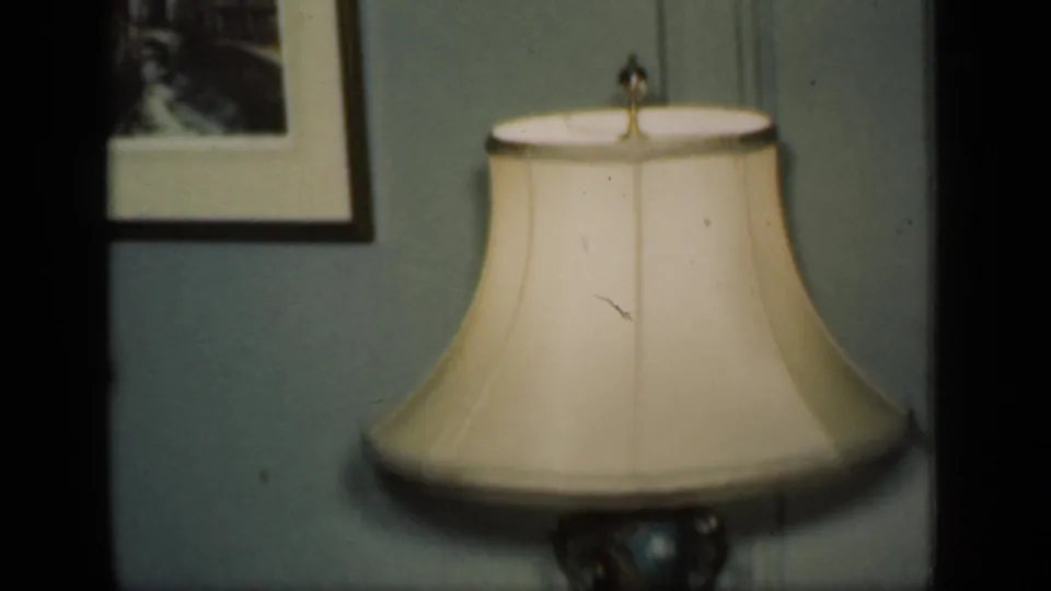 The final frame centers a cream-shaded lamp with a decorative base beneath framed wall art in the 1949 New York interior.