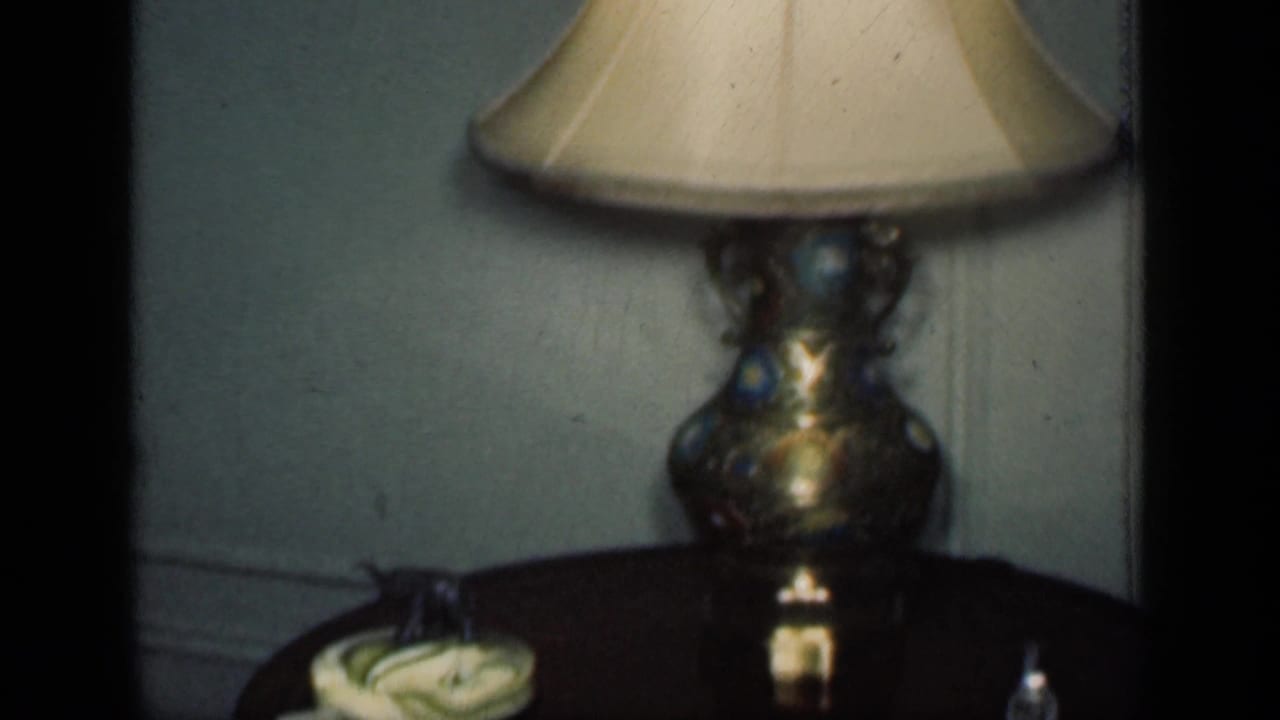 Table lamp with cream shade beside a round wooden table in a dim interior.