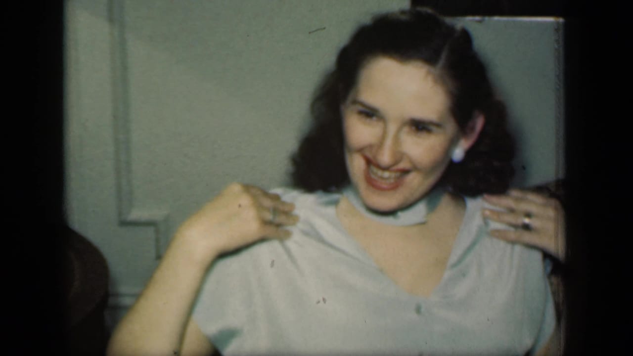 Woman smiling on a brown sofa while holding her blouse near her shoulders.